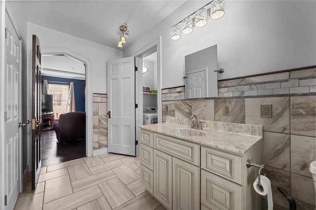 bathroom featuring tile walls, wainscoting, vanity, and washer / clothes dryer
