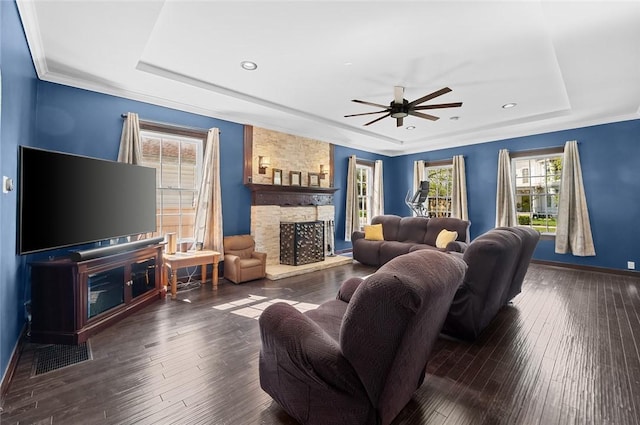 living room featuring hardwood / wood-style flooring, a stone fireplace, ceiling fan, and a raised ceiling