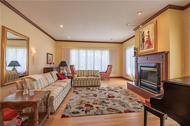 living room with recessed lighting, ornamental molding, a glass covered fireplace, and light wood-style flooring