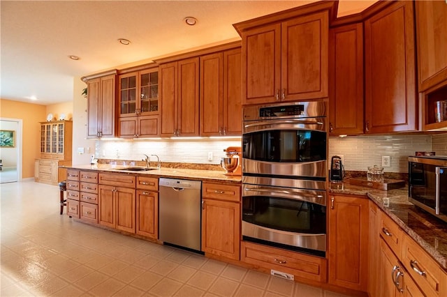 kitchen with dark stone countertops, a sink, decorative backsplash, brown cabinetry, and appliances with stainless steel finishes