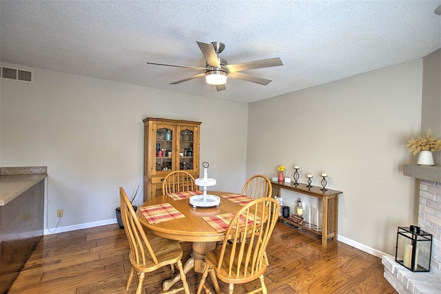 dining room featuring a textured ceiling, a fireplace, ceiling fan, and dark wood-type flooring