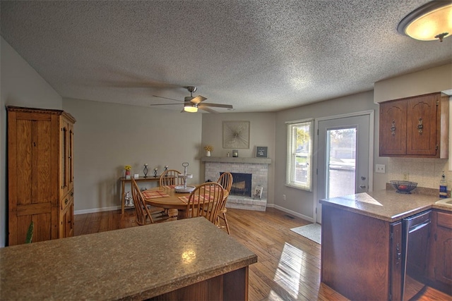 kitchen featuring a brick fireplace, stainless steel dishwasher, a textured ceiling, ceiling fan, and light hardwood / wood-style flooring