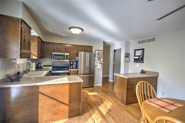 kitchen featuring backsplash, sink, light hardwood / wood-style flooring, kitchen peninsula, and stainless steel appliances