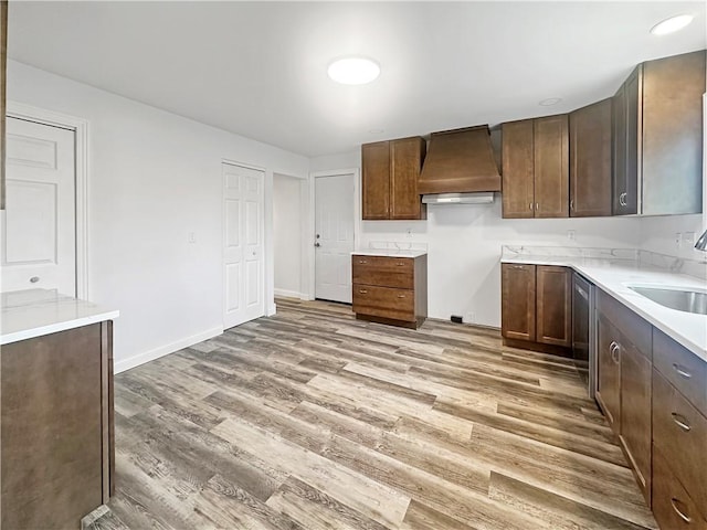 kitchen featuring a sink, wood finished floors, light countertops, baseboards, and custom exhaust hood