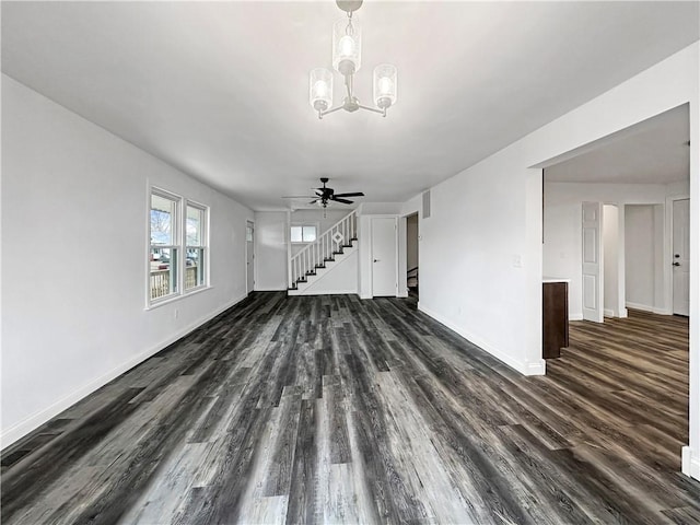 unfurnished living room featuring dark wood finished floors, ceiling fan with notable chandelier, stairs, and baseboards