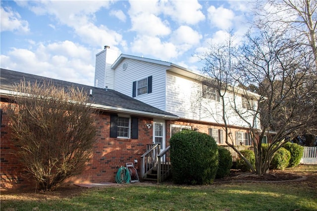 rear view of property featuring brick siding, a shingled roof, fence, a yard, and a chimney