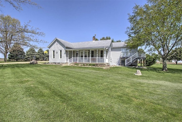 rear view of property with a lawn, covered porch, a chimney, and stairs