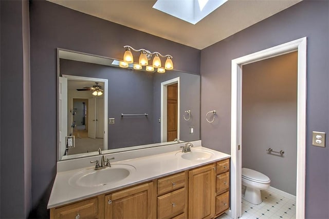 bathroom featuring a skylight, a sink, toilet, and double vanity