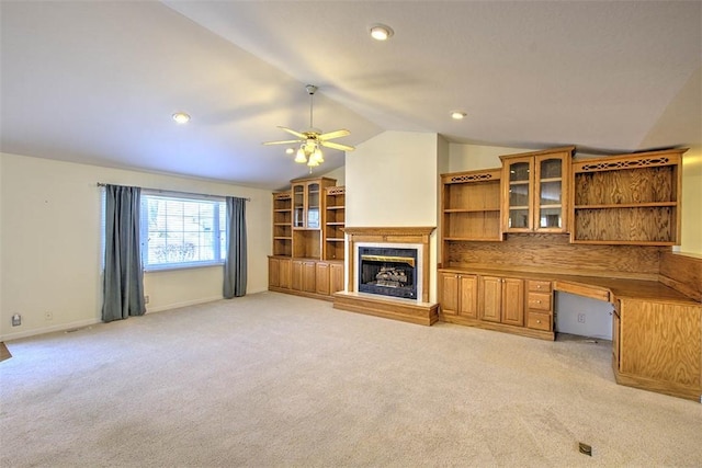 unfurnished living room featuring light colored carpet, a fireplace with raised hearth, built in study area, vaulted ceiling, and baseboards