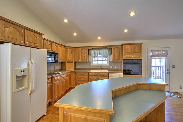 kitchen featuring a center island, lofted ceiling, light wood-style flooring, a sink, and black appliances