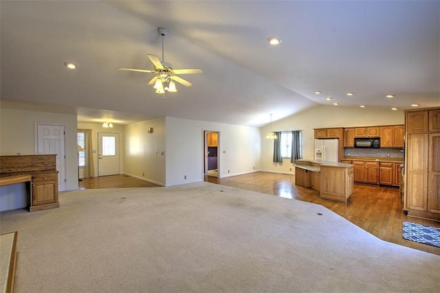 unfurnished living room featuring a ceiling fan, vaulted ceiling, light carpet, and plenty of natural light