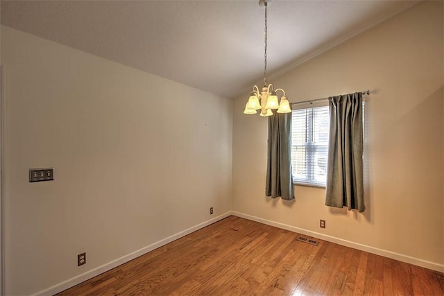 spare room featuring visible vents, an inviting chandelier, vaulted ceiling, wood finished floors, and baseboards