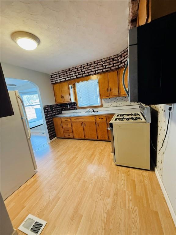 kitchen with brown cabinets, light countertops, visible vents, light wood-type flooring, and white appliances