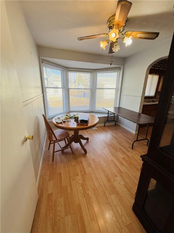 dining area with light wood-style floors, baseboards, arched walkways, and ceiling fan