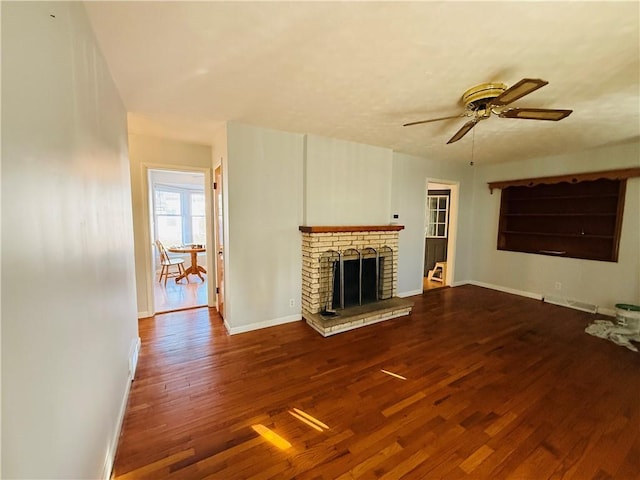 unfurnished living room with ceiling fan, a brick fireplace, wood finished floors, and baseboards