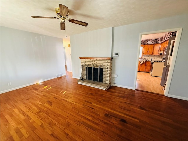 unfurnished living room with light wood-style flooring, visible vents, a ceiling fan, baseboards, and a brick fireplace