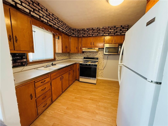 kitchen with gas range, stainless steel microwave, brown cabinets, freestanding refrigerator, and under cabinet range hood