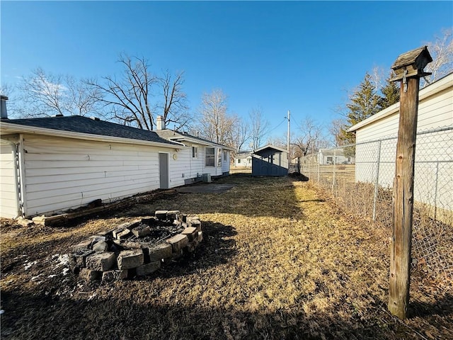 view of yard featuring an outbuilding, fence, a fire pit, and a shed