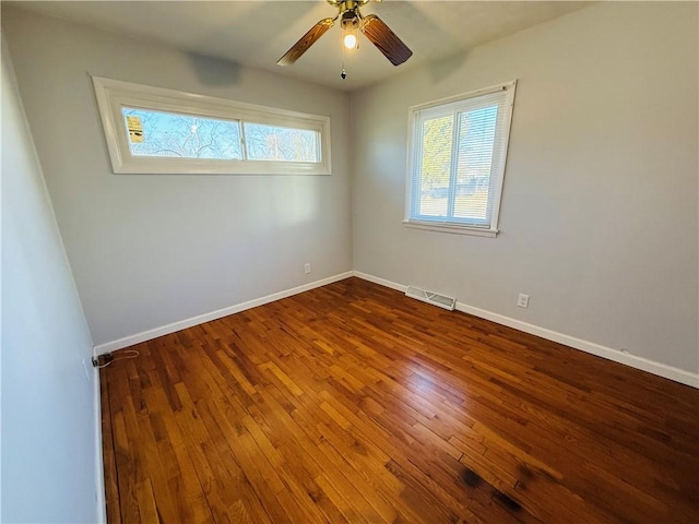 empty room featuring dark wood-style floors, visible vents, ceiling fan, and baseboards