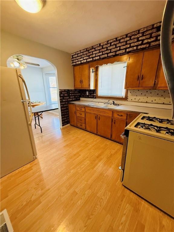 kitchen featuring white appliances, arched walkways, brown cabinets, and a sink