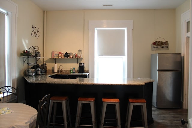 kitchen featuring light stone countertops, stainless steel fridge, kitchen peninsula, a kitchen breakfast bar, and dark hardwood / wood-style floors