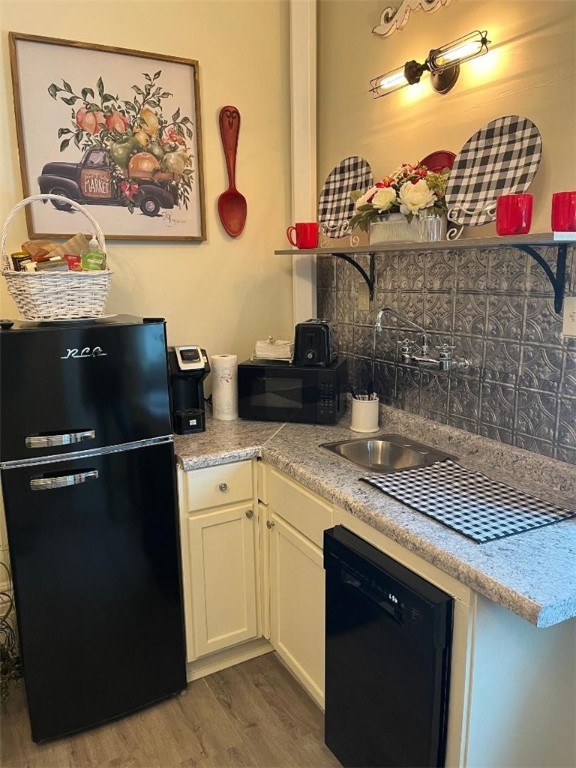 kitchen with black appliances, backsplash, sink, and hardwood / wood-style floors