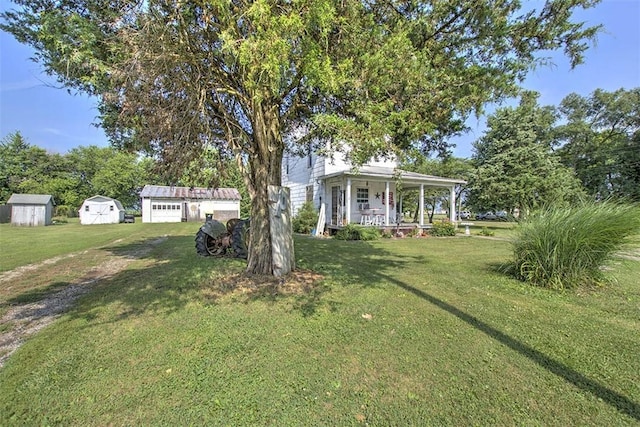 59 Lynn St, Weldon, IL 61882 - view of green lawn with covered porch, a storage shed, and a detached garage