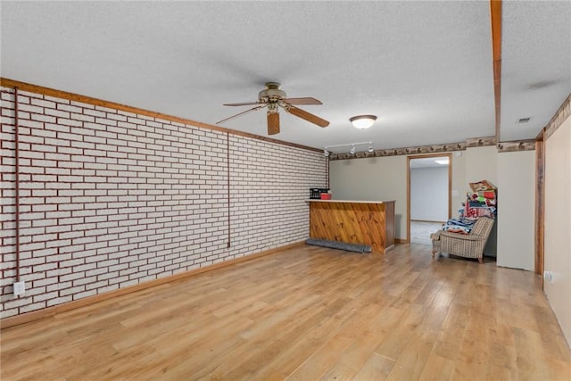 empty room with wood finished floors, brick wall, a ceiling fan, a textured ceiling, and a dry bar