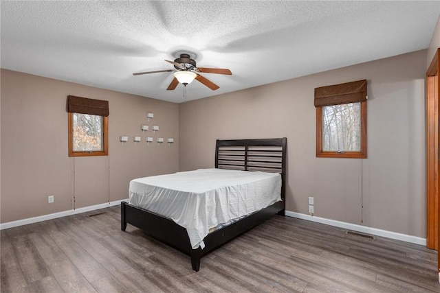 bedroom with a textured ceiling, wood finished floors, visible vents, and baseboards