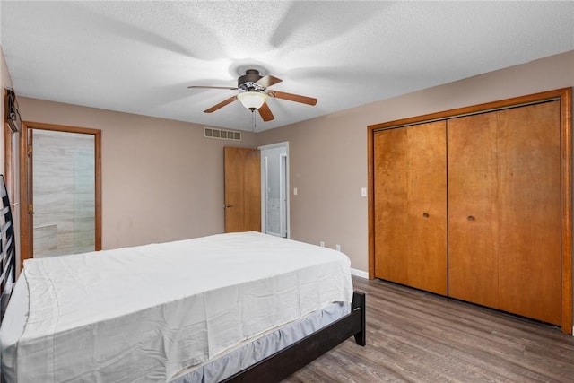 bedroom with wood finished floors, a closet, visible vents, a ceiling fan, and a textured ceiling
