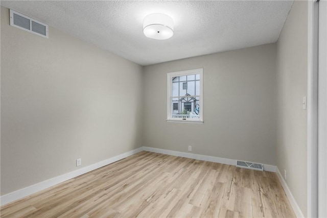 spare room featuring light wood finished floors, a textured ceiling, and baseboards