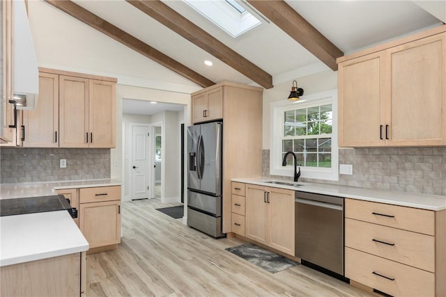 kitchen with light brown cabinets, stainless steel appliances, a sink, a skylight, and tasteful backsplash
