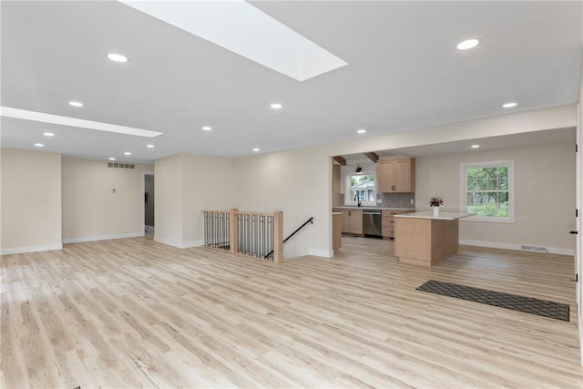 unfurnished living room featuring light wood finished floors, recessed lighting, a skylight, baseboards, and a sink