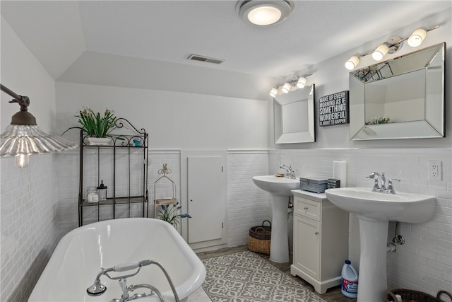 bathroom with a tub to relax in, lofted ceiling, double sink, and tile walls