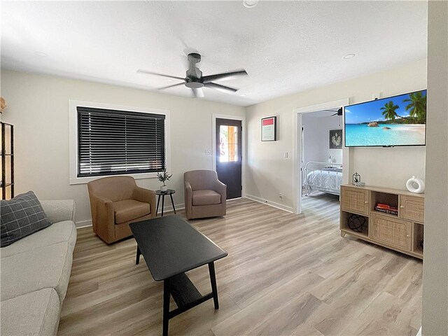 living area featuring light wood finished floors, ceiling fan, baseboards, and a textured ceiling