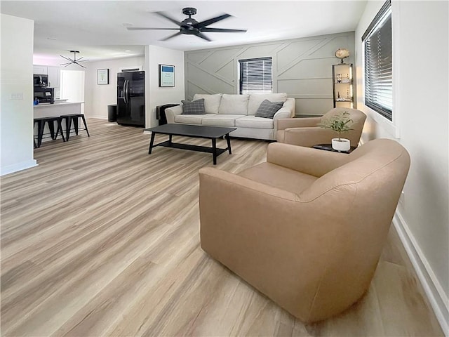 living area featuring ceiling fan, a decorative wall, light wood-type flooring, and baseboards