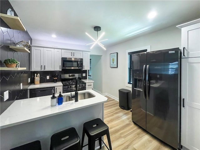 kitchen featuring light wood-style flooring, appliances with stainless steel finishes, a breakfast bar, open shelves, and backsplash