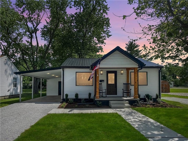 view of front facade featuring metal roof, an attached carport, a porch, a yard, and driveway