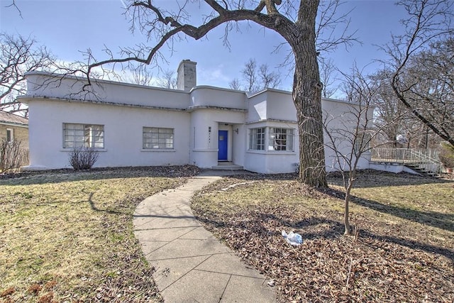 art deco inspired home with stucco siding, a front yard, and a chimney