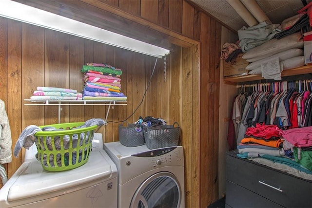 clothes washing area featuring washer and dryer, laundry area, and wooden walls