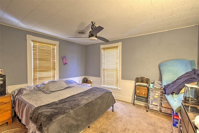 bedroom with ceiling fan, carpet flooring, visible vents, and wainscoting