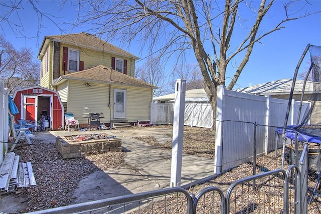 back of house with roof with shingles, a fenced backyard, entry steps, an outdoor structure, and a storage shed