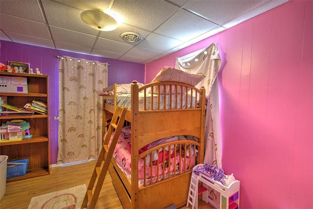 bedroom with a drop ceiling, visible vents, and wood finished floors