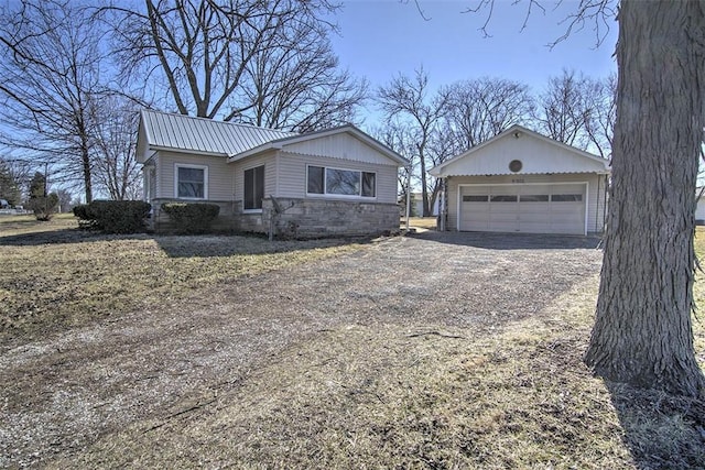 ranch-style house with dirt driveway, metal roof, a garage, an outdoor structure, and stone siding