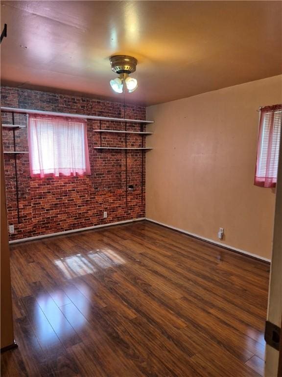 unfurnished room with baseboards, ceiling fan, wood finished floors, and brick wall
