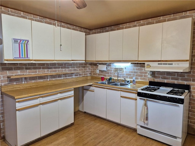 kitchen with gas range gas stove, a sink, white cabinets, under cabinet range hood, and light wood-style flooring