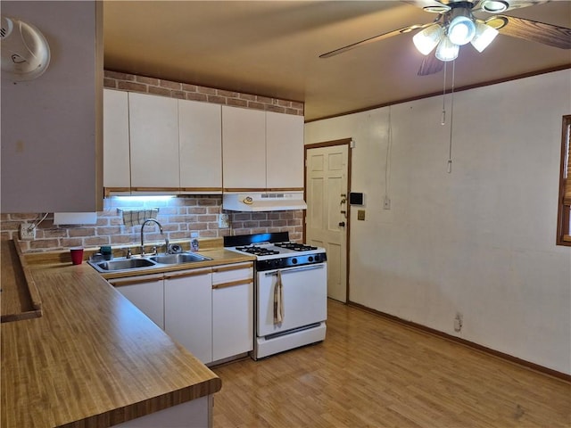 kitchen with white gas stove, a ceiling fan, a sink, white cabinets, and under cabinet range hood