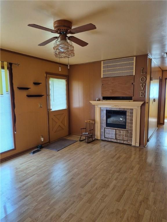 unfurnished living room featuring baseboards, ceiling fan, a tile fireplace, and wood finished floors
