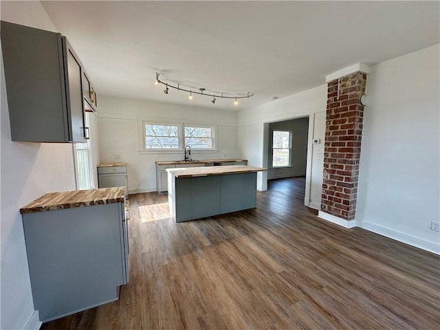 kitchen with sink, butcher block countertops, dark wood-type flooring, gray cabinets, and a center island