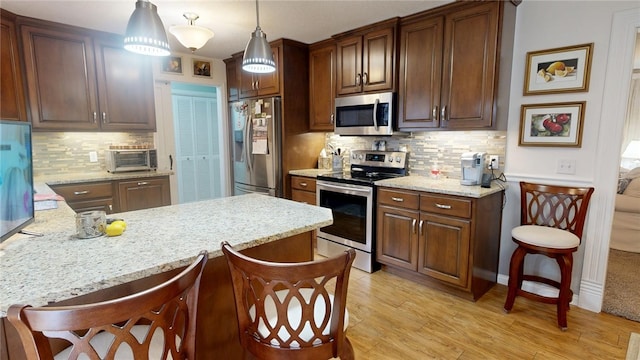 kitchen with appliances with stainless steel finishes, light wood-type flooring, backsplash, and light stone counters